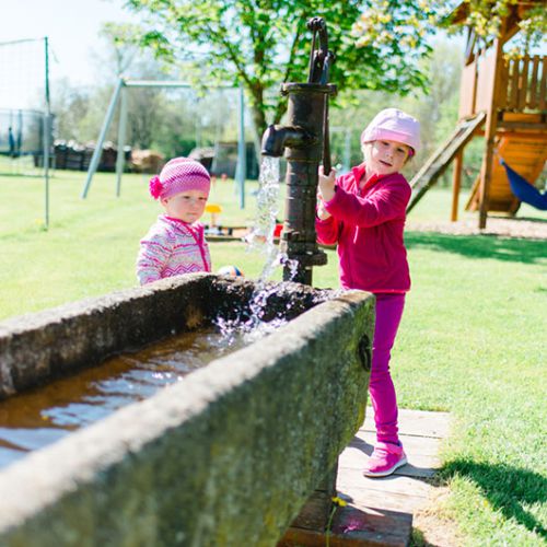 Zwei kleine Mädchen spielen mit einer Wasserpumpe