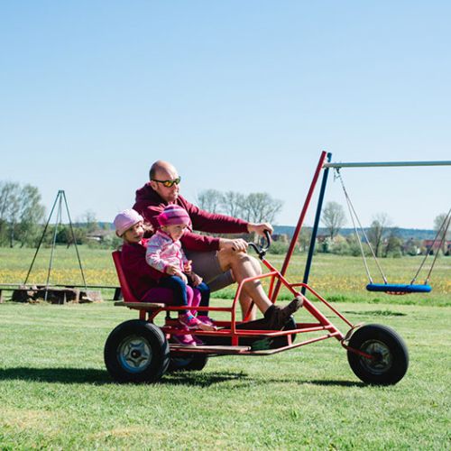 Vater fährt mit 2 Kindern auf dem Kettcar auf der Wiese