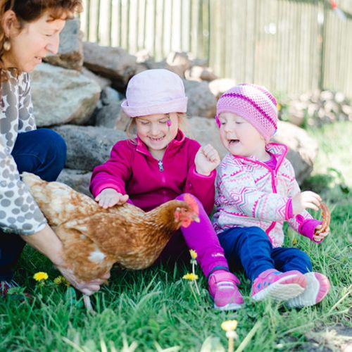 Zwei Mädchen spielen mit einem Huhn