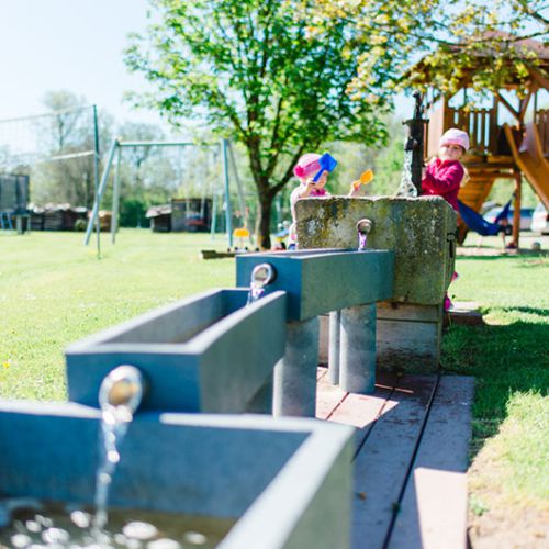 Kleines Mädchen spielt mit einer Wasserpumpe