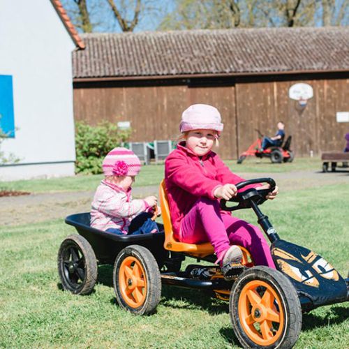Zwei Kinder fahren mit dem Kettcar auf der Wiese